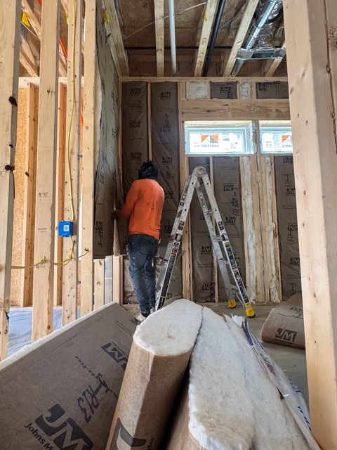 Installer fitting fiberglass insulation into an open wall cavity.