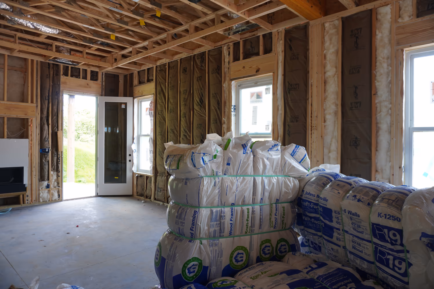 Fiberglass insulation bags staged inside a framed room before installation.