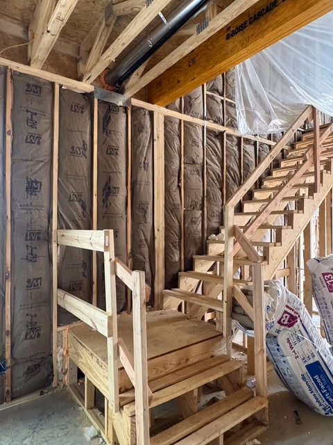 Fiberglass insulation installed along a stair wall before the next trade arrives.