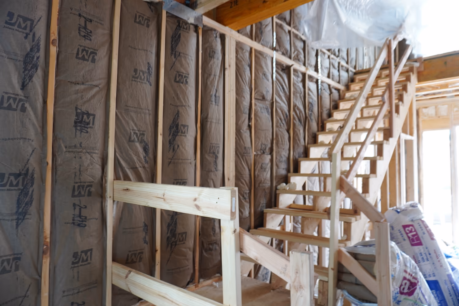 Fiberglass insulation installed around stairwell framing and wall lines.
