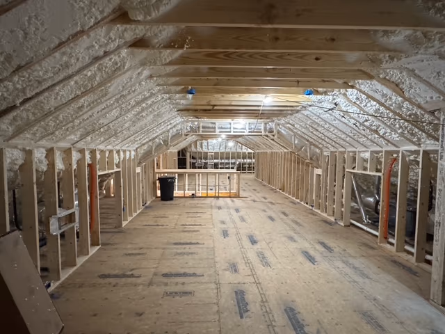 Spray foam installed across an attic roofline and framing bays.